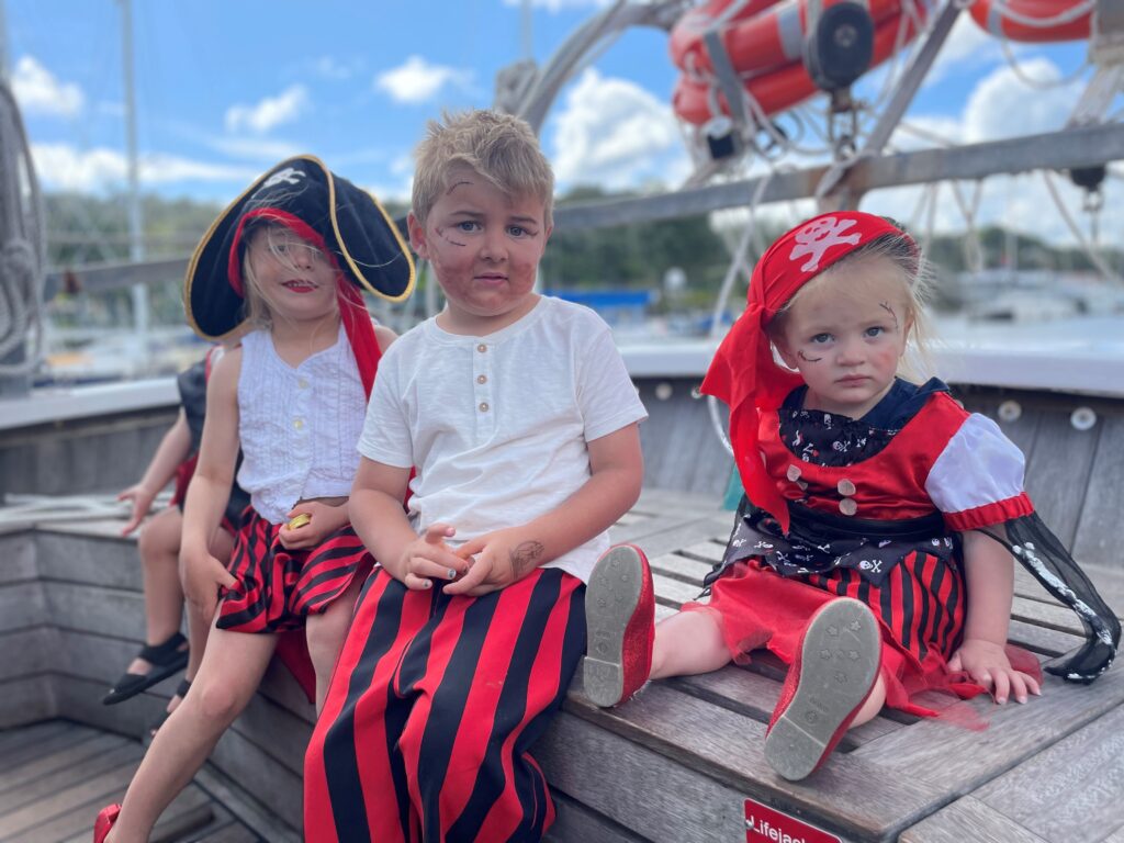 Three young children dressed in pirate costume sitting on a ship